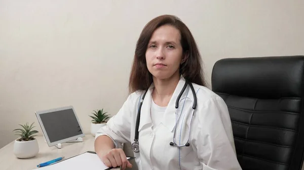 Family doctor has an online conversation. Smart female doctor in white coat and stethoscope using laptop to consult patient remotely in hospital office. Telemedicine. Online appointment with a doctor. — Stock Photo, Image