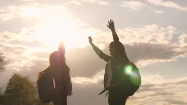 Özgür kız gezginler zıplar ve güneş ışınlarıyla sevinirler. Sırt çantalı kadın turistler tepenin üstünde buluşmuşlar. Takım çalışması, yürüyüş. Zorlukların üstesinden gelmek için hareket et. Zafer ve başarının sevinci — Stok video