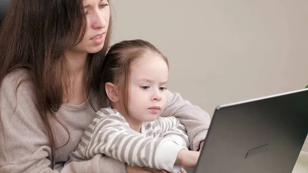 Mãe e bebê trabalham no computador como freelancer em casa remotamente. A mãe trabalha com um laptop e brinca com a filhinha. A mãe a trabalhar e a criar filhos. Mulher de negócios no escritório com criança — Fotografia de Stock