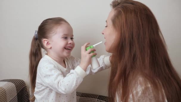 La mamma gioca e tratta i bambini raffreddore e gola spruzzando medicina in bocca babys. Il bambino gioca e fornisce cure mediche alla madre malata. Mamma si sta prendendo cura del bambino con l'influenza. Spray per gola — Video Stock