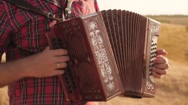 İnsan güneşte akordeon çalar. Neşeli bir adam müzik aleti çalıyor. Sanatçı açık havada şarkı söyler ve enstrüman çalar. Kırsalda gelenek ve kutlama.