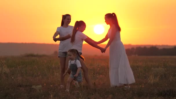 Здоровая семья играет на траве на закате в парке. Молодая мать со здоровыми дочерьми играет вместе, танцует в кругу на солнце, веселится на поле. Концепция счастливого семейного детства — стоковое видео