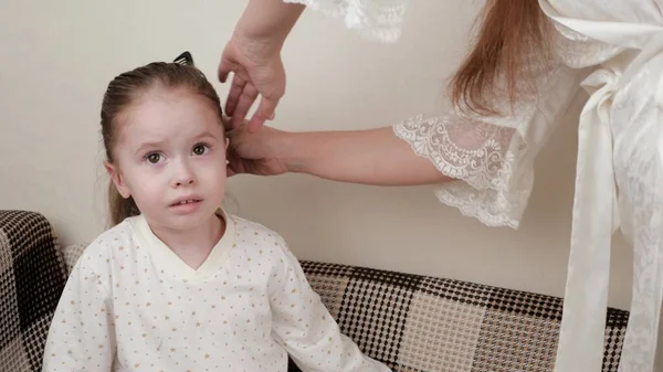 Mom combs her beloved daughters hair with a comb before bed. Healthy child in pajamas. A beautiful hairstyle for a cute daughter. Happy family. Mom braids her little daughters braid. — Stock Photo, Image