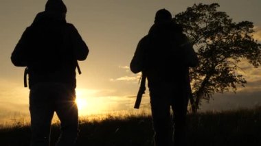 Yürüyüşçüler gün batımında yürüyorlar. Güneşte yapayalnız bir ağacın yanından geçen iki yolcunun silueti. Yol boyunca sırt çantalı turistlerin takım çalışması. Yürüyüş ve açık hava macerası, park, alan.