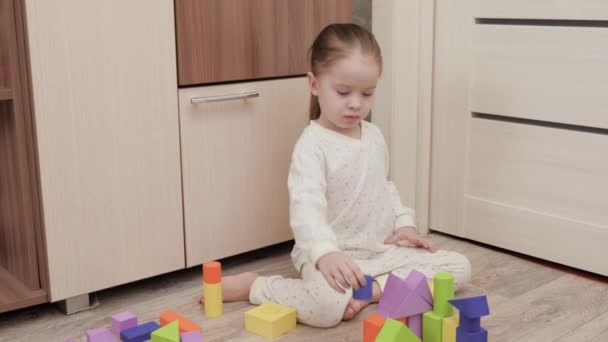 Kind speelt met gekleurde blokjes in kinderkamer op de vloer. Het kind bouwt een familiehuis. Educatieve spelletjes voor de ontwikkeling van kinderen. Een kind onderwijzen door te spelen. Gelukkige familie, dochter. — Stockvideo