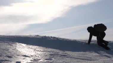 Turistlerin takım çalışması, zafer için çabalaması. Yürüyüşçüler, arkadaşının karlı dağa tırmanmasına yardım ediyor. Kış mevsiminde gezginlerin silueti parlak güneş ışınlarıyla tepede. Spor turizmi
