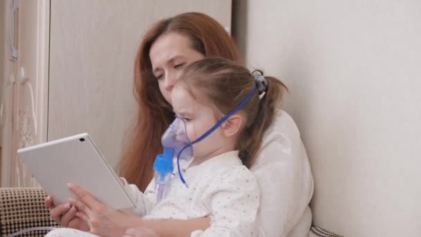 Lecz swoje dziecko na przeziębienia w domu. Mama leczy córkę inhalacją i razem oglądają kreskówki na tablecie. Dziecko otrzymuje terapię oddechową z nebulizatorem. Dziecko cierpi na kaszel. — Wideo stockowe