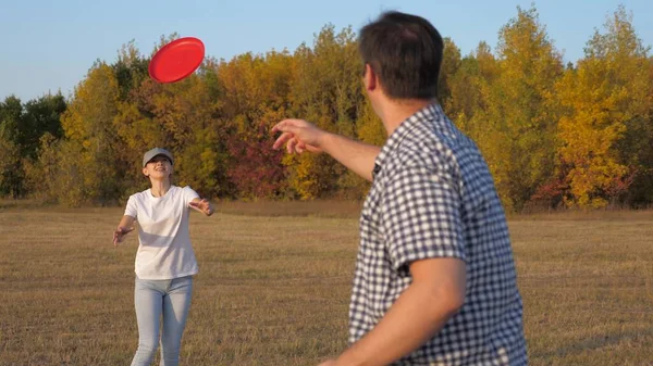 Lycklig familj, man och kvinna spelar, kastar en flygande röd skiva till varandra i parken. Ett sorglöst par, unga människor som har roligt tillsammans. Sport och ungdom. Spela utomhus. — Stockfoto