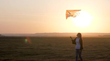 Kız, güneş ışınlarıyla tarlada çok renkli bir uçurtmayla oynuyor. Gençler uçmayı ve pilot olmayı hayal ederler. Renkli uçurtma havada asılı duruyor. Uçurtma Festivali. Yazın gün batımında çocuk ve uçan uçurtma.