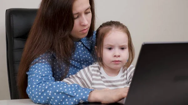 Frilansare Mamma och barn arbetar på datorn på distans hemma. Mamma jobbar med en laptop och leker med sin dotter. Mamma jobbar och uppfostrar barn. Affärskvinna i ämbetet med barn — Stockfoto