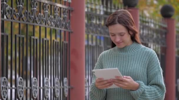 Dziewczyna używająca tabletu cyfrowego drukuje wiadomości na ulicy. Studentki dotykają tabletów dotykiem. Kobieta pracuje z tabletem, spacerując po chodniku w mieście. — Wideo stockowe