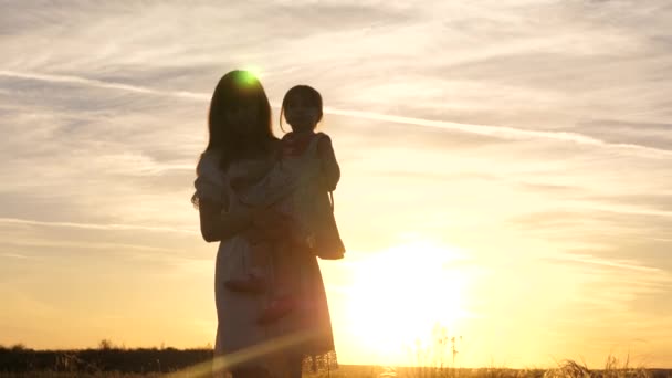 Mamusia idzie ze swoją córeczką w ramionach na polu w słońcu. Szczęśliwa rodzina, dzieciństwo. Mama i córka bawią się w parku w weekend. Szczęśliwe dziecko bawiące się z matką o zachodzie słońca. Dziecko kocha mamę. — Wideo stockowe
