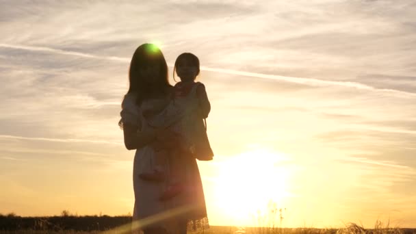 Mamma går med sin lilla dotter i armarna i solen. Lycklig familj, barndom. Mamma och dotter leker i parken på helgen. Glada barn leker med sin mamma vid solnedgången. Baby älskar mamma — Stockvideo