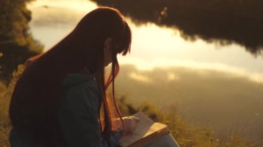Kız öğrenci nehrin yanındaki parkta bir kitap okuyor. Kadın dışarıda İncil okuyor. Kız dağın tepesinde dersler veriyor. Kendi kendini eğitme konsepti. Kutsal kitaplarda gerçeği aramak..