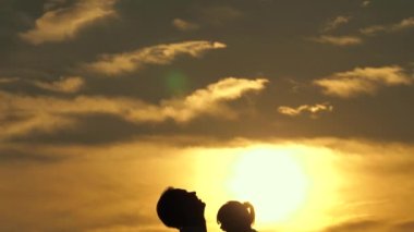 Baba ve küçük çocuk birlikte oynuyorlar, gülüyorlar ve sarılıyorlar. Babam mavi gökyüzüne mutlu bir kız çocuğu fırlatıyor. İyi yolculuklar. Bebeğin ebeveynin kollarında olması. Baba izinli. Mutlu bir aile kavramı. Siluet