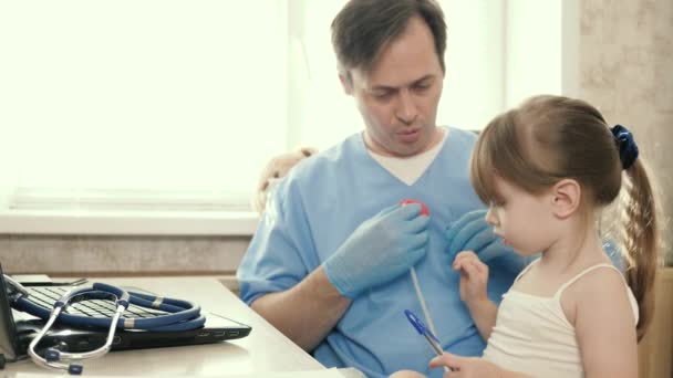 Cuidar a un pediatra profesional masculino jugando con un niño pequeño en la oficina. Un pediatra ve a un niño pequeño. El médico escucha al corazón de los niños con un estetoscopio. Clínicas privadas. — Vídeos de Stock