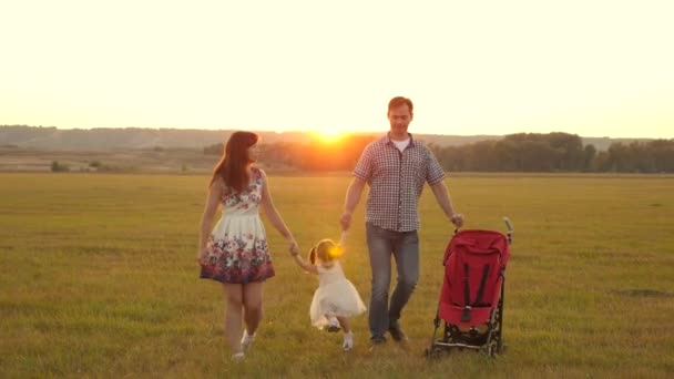 Lycklig familj, barn leker med pappa och mamma på fältet i solsken. Lilla dottern leker och hoppar med pappa och mamma i parken vid solnedgången. Vandring med ett litet barn i naturen, barnvagn — Stockvideo