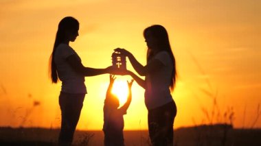 Aile oyunları, ev hayalleri, sağlık ve günbatımında aşk. Mutlu aile anne ve çocukları kendi elleriyle bir eyer evi tutuyorlar. Genç aileler için kredi ve emlak sigortası kavramı.