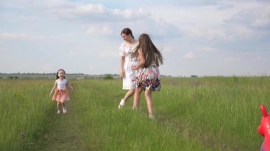 Mutlu çocuklar, bebek ve anne baharda parkta birlikte koşarlar. Mutlu aile yazın yeşil çimlerde çayırda koşar ve oynar. Kardeşler ve annem arayı kapatır. Çocuk neşeyle kaçıyor. Takım çalışması.