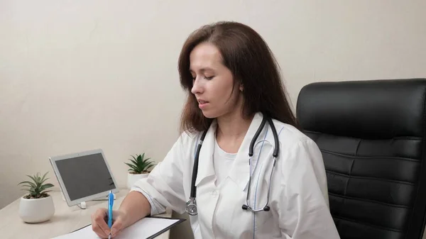 Family doctor has an online conversation. Online appointment with a doctor. Smart female doctor in white coat and stethoscope using laptop to consult patient remotely in hospital office. Telemedicine.