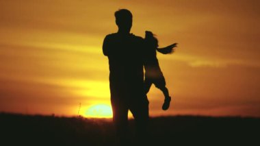 Baba, sevgili kızının etrafında güneş ışınlarıyla dönüyor. Mutlu aile, gün batımında bir tarlada baba ve kız. Baba ve küçük kızı birlikte oynuyorlar. Mutlu aile ve sağlıklı çocukluk kavramı