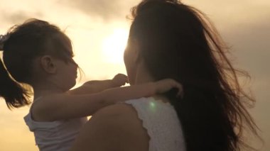 Anne ve şirin bebek güneşte sarılıyor. Mutlu aile anne ve kızı gün batımında tarlada. Anne ve kızı güneşle oynayarak ellerini uzatıyorlar. Mutlu aile ve sağlıklı çocukluk kavramı