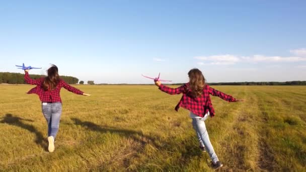 Мрії про політ. Щаслива концепція дитинства. Дві дівчини грають з іграшковим літаком на заході сонця. Діти на фоні сонця з літаком в руці. Силует дітей, які грають у літаку — стокове відео