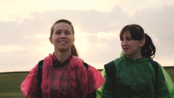 Viaggiatrici in impermeabili e zaini colorati. Lavoro di squadra. I turisti femminili liberi camminano giù la collina nella valle bella che tiene per mano. avventura e concetto di viaggio. Turisti donne sane viaggiano. — Video Stock