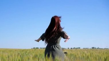 Mutlu genç kız tarlada ağır çekimde koşuyor, buğday başaklarına eliyle dokunuyor. Güzel, özgür bir kadın günbatımı arka planındaki buğday tarlasında güneşin altında doğanın tadını çıkarıyor. Kız seyahat eder.