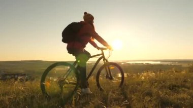 Bisikletli bir yolcunun kadını, manzaraya ve güneşin doğuşuna hayran kalarak dağın kıyısında yol alır. Bedava turist güneşin altında bisiklet sürüyor. Spor yaşam tarzı. Egzersiz yapan bisikletçi