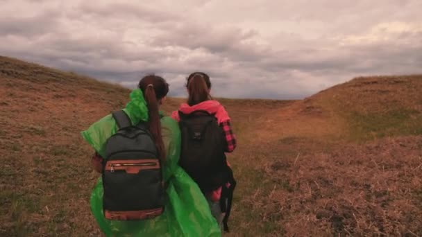 Giovani donne felici in impermeabili colorati viaggiano con zaini nel burrone. Belle ragazze turisti vanno insieme in cerca di avventura. Lavoro di squadra. In un giorno libero nella natura. Sane passeggiate all'aperto — Video Stock