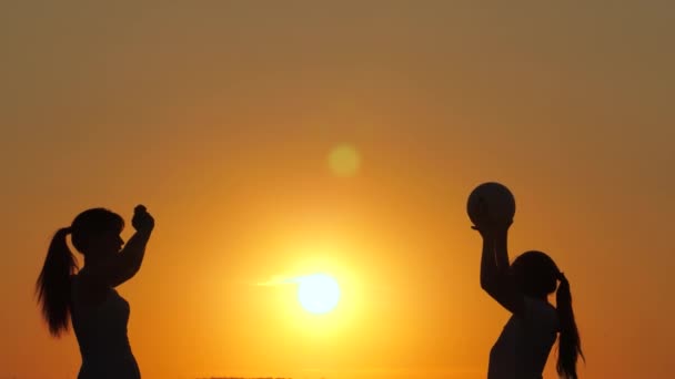 Feliz familia de vacaciones, mamá y su hija juegan pelota en la playa bajo el sol. Niños sanos y felices jugando con voleibol al atardecer. Familia feliz y concepto de infancia. Camping familiar en verano — Vídeo de stock