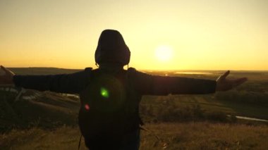 Sırt çantalı gezgin şafak vakti dağın kenarında duruyor, ellerini kaldırıyor ve zaferin, güneşin ve manzaranın tadını çıkarıyor. Bedava turist güneşte tek başına seyahat eder. Macera ve keşif kavramı