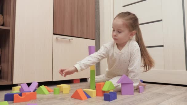 Kind meisje speelt met gekleurde kubussen in kinderkamer op de vloer. Hij bouwt een familiehuis. Educatieve spelletjes voor de ontwikkeling van kinderen. Een kind onderwijzen door te spelen. Gelukkige familie, dochter. — Stockvideo