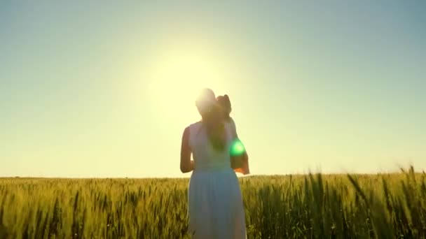 Mamma e figlioletta camminano in un campo di grano verde, abbracciandosi e baciandosi. Un bambino e una mamma camminano nel campo di grano. Buon viaggio in famiglia. Il bambino e 'tra le braccia delle mamme. Agricoltore donna e bambino in campo — Video Stock