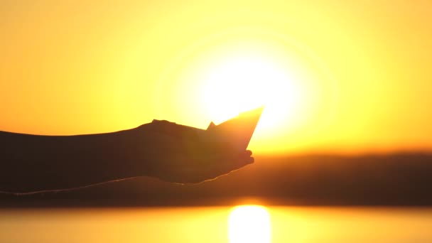 Рука Чайлдса держит игрушечную бумажную лодку в лучах солнца. Парень играет с лодкой. Путешествия и приключения. Игры на свежем воздухе для детей. Счастливая семья в отпуске. Бизнес в хороших руках — стоковое видео