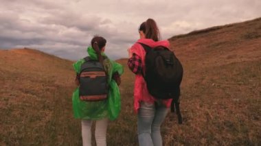 Güzel kız turistler macera aramak için birlikte giderler. Renkli yağmurluk giyen mutlu genç kadınlar sırt çantalarıyla vadide seyahat ederler. Takım çalışması. Doğada boş bir günde. Sağlıklı doğa yürüyüşleri.