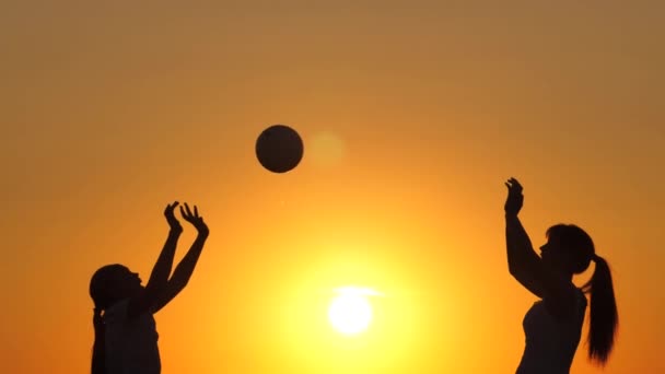 Ευτυχισμένα υγιή παιδιά που παίζουν με μια μπάλα στο ηλιοβασίλεμα. Χαρούμενη οικογένεια και παιδική ηλικία. Η μαμά και η κόρη παίζουν και παίζουν μπάλα ο ένας στον άλλο κάτω από τον ζεστό ήλιο. Διασκέδαση οικογενειακό κάμπινγκ το καλοκαίρι — Αρχείο Βίντεο