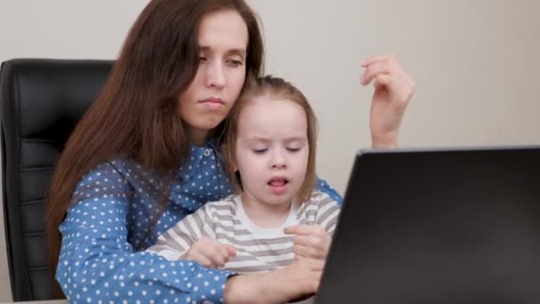 Moe moeder werkt met een laptop en speelt met haar dochtertje. Mam werkt en voedt kinderen op. Zakenvrouw in functie met een kind. Werken aan een computer als freelancer thuis op afstand. — Stockvideo