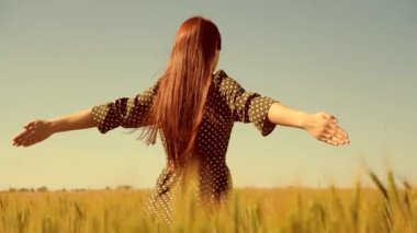 Mutlu genç kız tarlada ağır çekimde koşuyor, buğday başaklarına eliyle dokunuyor. Güzel, özgür bir kadın günbatımı arka planındaki buğday tarlasında güneşin altında doğanın tadını çıkarıyor. Kız seyahat eder.