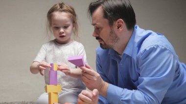Baba ve kızı yerdeki çocuk odasında renkli küplerle oynuyorlar. Baba ve kızı aile evi inşa ediyorlar. Çocuğa oyun aktiviteleri öğretmek. Mutlu bir aile. Çocuklar için eğitici oyunlar