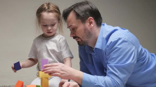 Ojciec i córka bawią się w kolorowe kostki w pokoju dziecięcym na piętrze. Tata i córka budują dom rodzinny. Uczenie dziecka poprzez zabawę. Szczęśliwa rodzina. Gry edukacyjne dla dzieci — Wideo stockowe