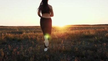Güneşin peşinden koşmak. Antrenman koşusu. Sağlıklı, güzel bir kız spor yapıyor, kırsalda güneş altında koşuyor. Koşucu kız sahada temiz hava soluyor. Özgür genç kadın gün batımında yaz parkında koşuyor..