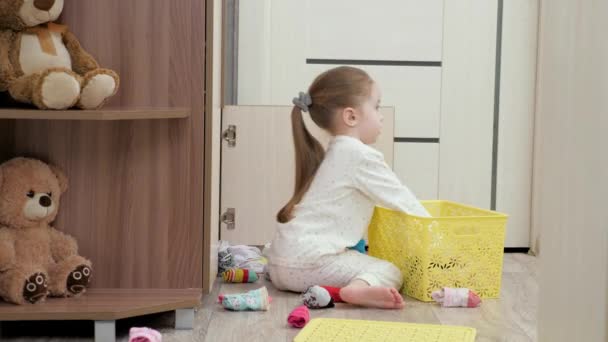 El chico juega y tira sus cosas de la caja. La hija juega con la ropa en casa. Un niño en pijama abre un armario y busca su ropa. Niña juega en la habitación de los niños. — Vídeos de Stock