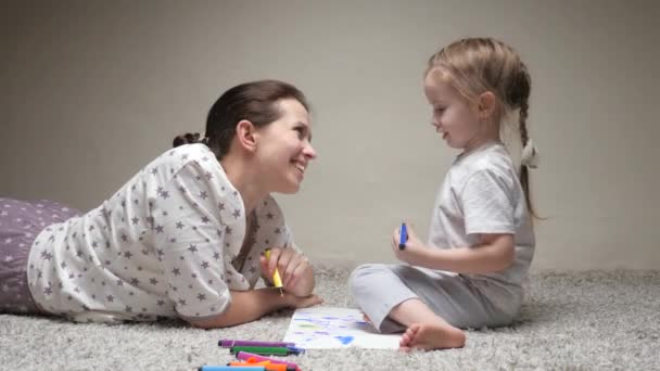 La mamma, la tata, insegna a disegnare alla bambina. Famiglia felice che gioca insieme a casa sul pavimento. La mamma aiuta sua figlia a imparare a disegnare sulla carta colorando con matite multicolori e pennarelli.. — Video Stock