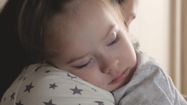 Bébé, l'enfant dort dans les bras de sa mère. Une jeune mère aimante embrasse sa douce fille adorable, qui s'endort dans ses bras. Genre, mère attentionnée et mignonne petite fille étreignant dans la chambre. — Video