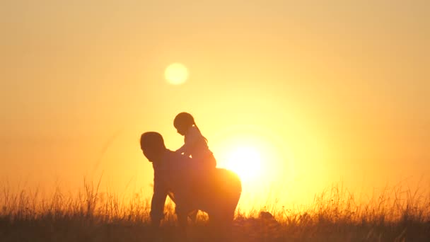 Família feliz. Papai brinca com sua filhinha no parque na grama em raios de pôr do sol. O pai rola o bebê de costas, ele se senta pai, se alegra. Papai e criança brincam na rua — Vídeo de Stock