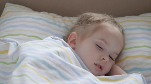Feliz bebé duerme en una cama de bebé y sonríe. Mamá acostó a su hija cansada. Un niño lindo está descansando en la guardería en su cama. Familia feliz y concepto de infancia. Niños sanos. — Vídeos de Stock