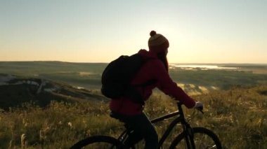 Bisikletli bir yolcunun kadını, manzaraya ve güneşin doğuşuna hayran kalarak dağın kıyısında yol alır. Bedava turist güneşin altında bisiklet sürüyor. Spor yaşam tarzı. Egzersiz yapan bisikletçi