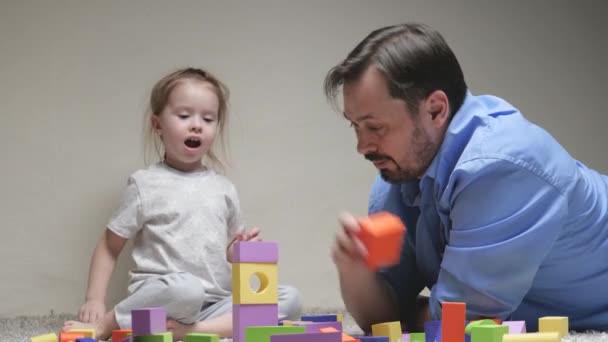 O pai e a filha estão a construir uma casa para a família. Família feliz. Jogos educativos para crianças. Pai e filha jogar cubos coloridos na sala das crianças no chão. Ensinar a criança através de atividades lúdicas — Vídeo de Stock